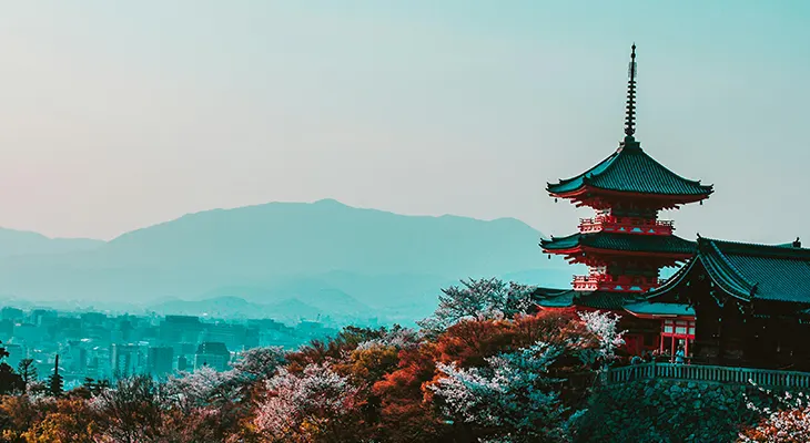 A red pagoda on a wooded hillside overlooking a city and distant mountains