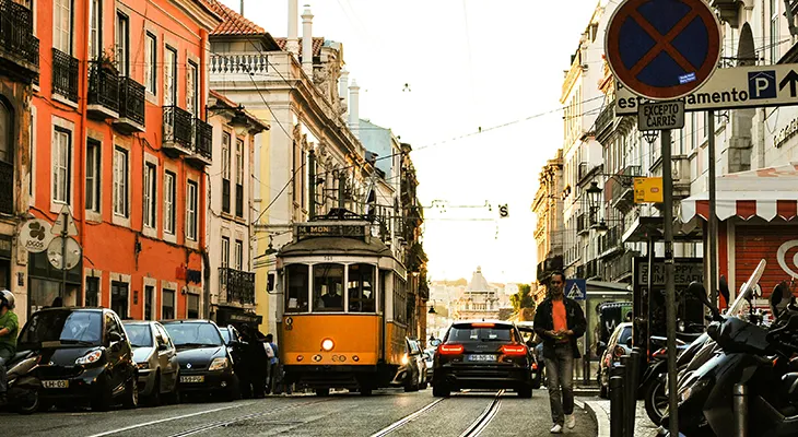 A yellow Lisbon tram on a street lined with parked cars and scooters