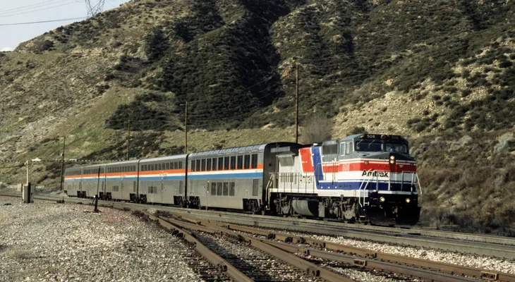 An Amtrak passenger train with a red, white and blue locomotive running through dry California hills