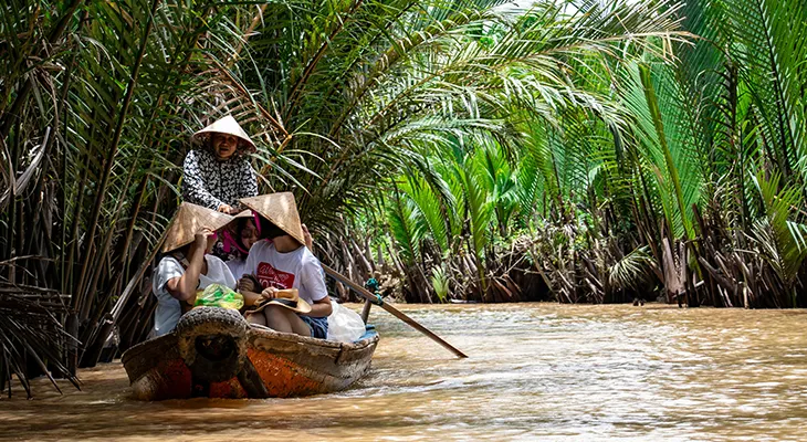 Visitors in conical hats on a small rowing boat in a palm-lined river channel