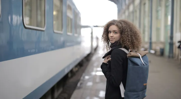 A woman with a backpack on a station platform beside a blue and white train, looking back over her shoulder